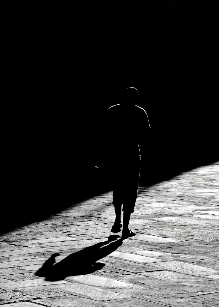 Strada urbana vuota con una sola persona che cammina tra le ombre.