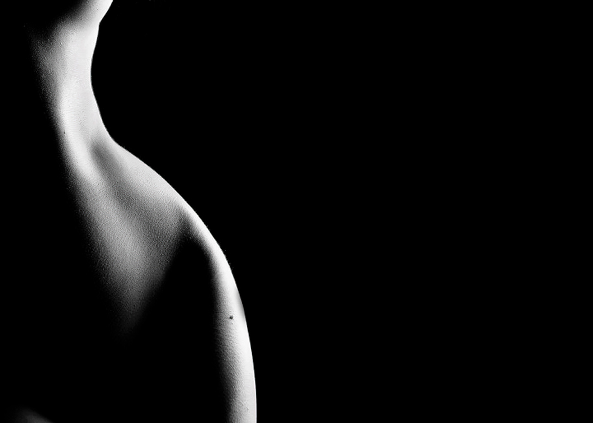 Schiena e spalla femminile illuminata su nero, fotografia corpo umano negative space minimalista Illuminated female back and shoulder on black, minimalist negative space human body photography