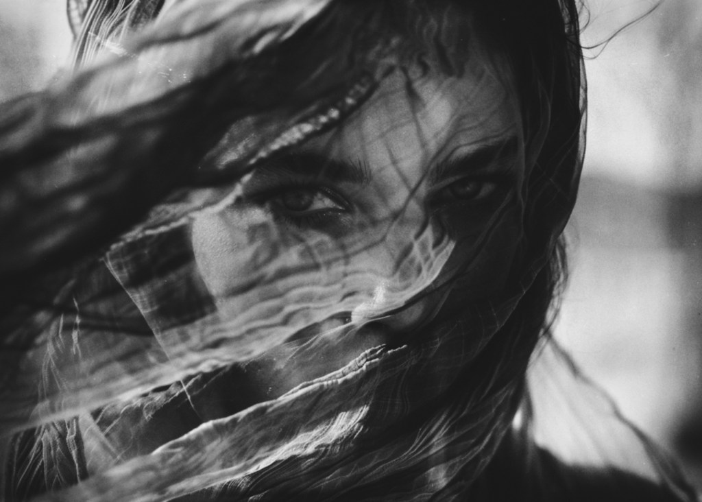 Ritratto in bianco e nero di una donna con velo mosso dal vento, texture sovrapposte e atmosfera onirica. Black and white portrait of a woman with a veil moved by the wind, layered textures and dreamlike atmosphere.