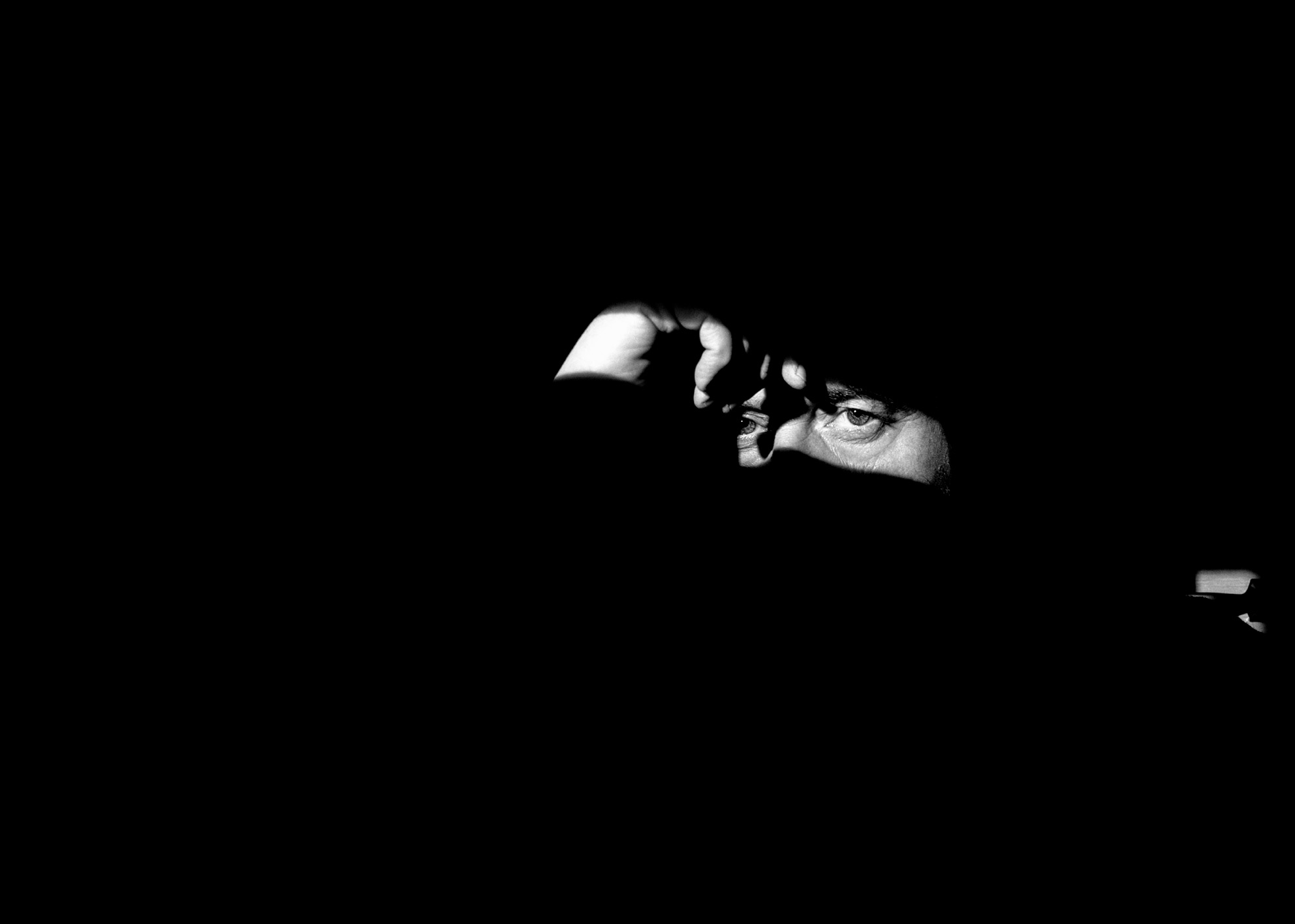 Volto maschile parzialmente illuminato emerge dal nero, identità rivelata dalla luce Male face partially illuminated emerges from black, identity revealed by light