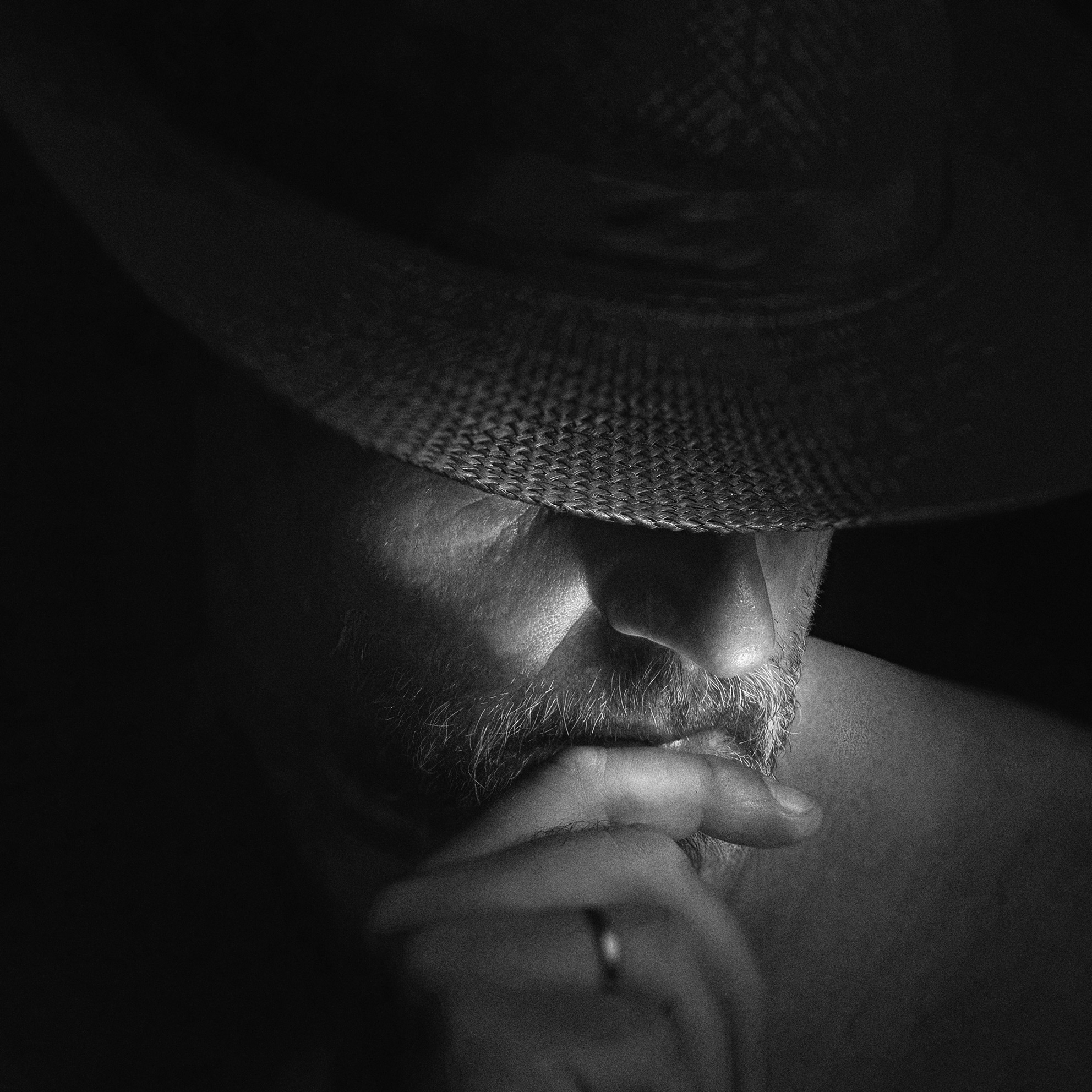 Ritratto in bianco e nero ravvicinato di un uomo con cappello e mano davanti alla bocca in atteggiamento riflessivo Close up black and white portrait of a man wearing a hat with hand in front of his mouth in a reflective mood