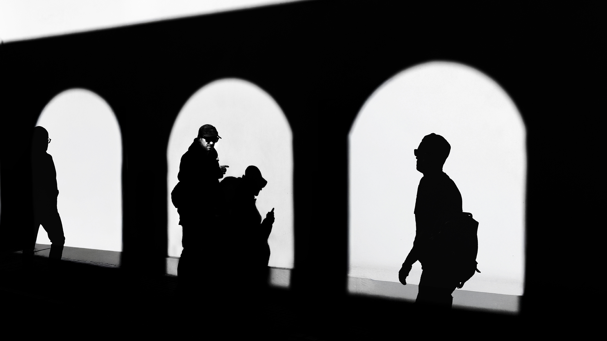 Silhouette di persone davanti a grandi aperture luminose, alcune osservano lo smartphone