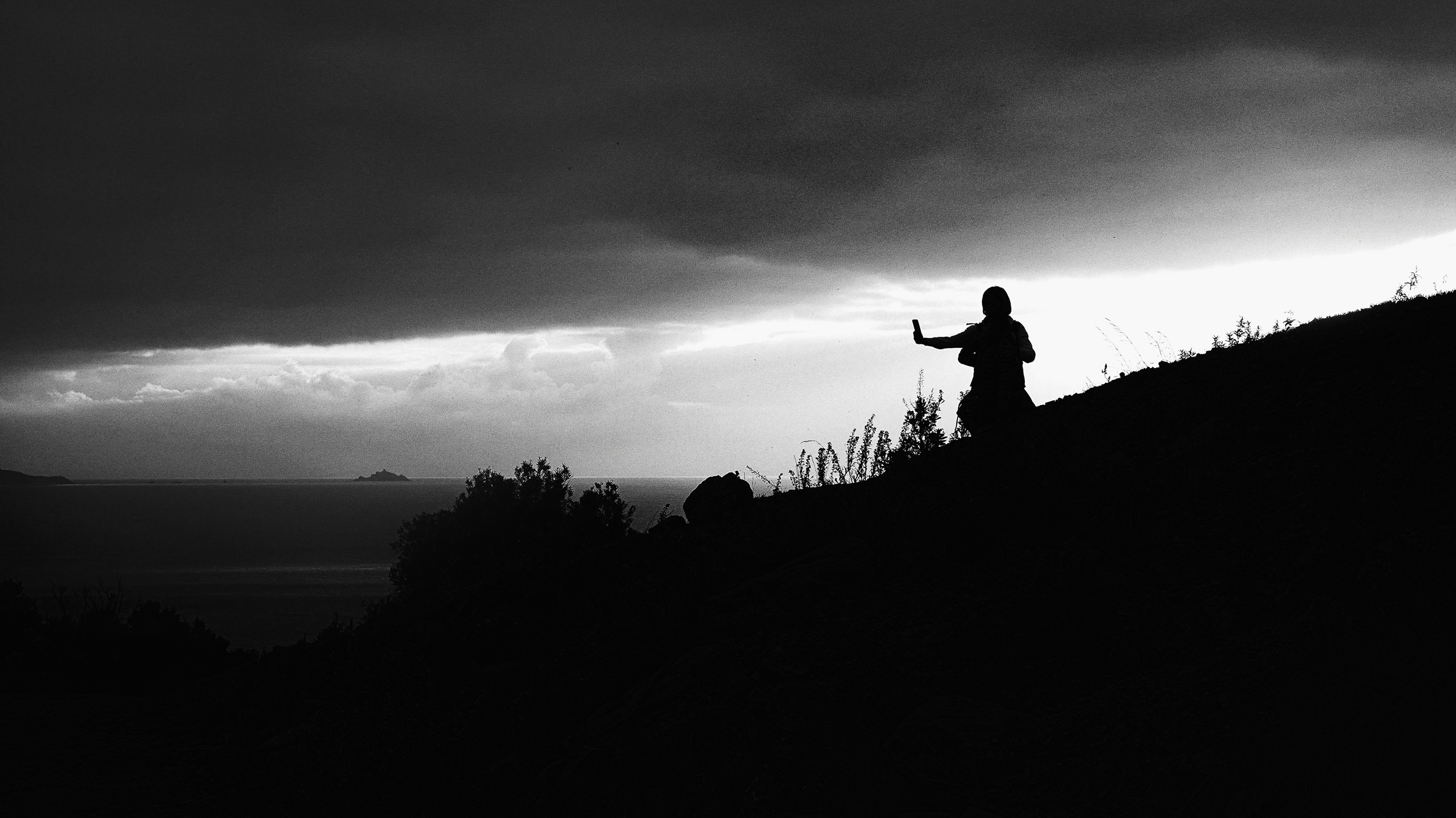 Persona in silhouette che fotografa con lo smartphone davanti a un paesaggio nuvoloso